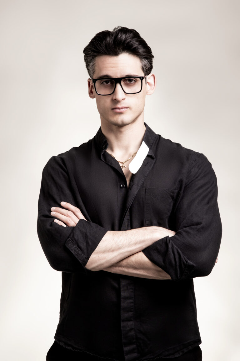 Ritratto di Alberto Ravagnani, protagonista dello spettacolo teatrale Una scelta, con camicia nera e occhiali, in posa frontale su sfondo neutro.